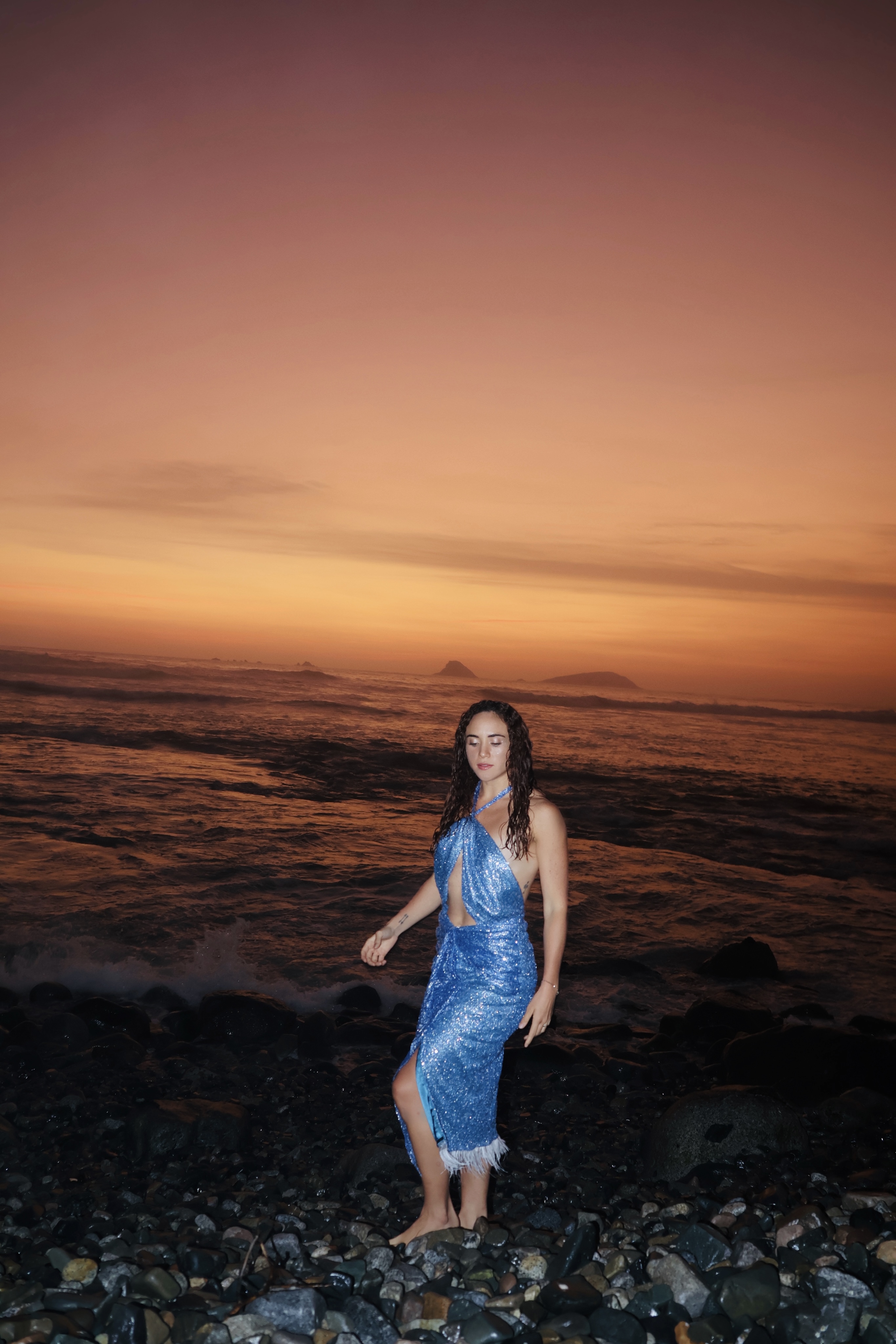 Vestido azul profundo de lentejuelas, con escote halter que envuelve el pecho y deja la espalda abierta al misterio.
La abertura lateral insinúa el movimiento de una ola, mientras las plumas blancas al final de la falda evocan un andar etéreo, como si el cuerpo flotara sobre la luz.
Inspirado en el poder sutil de las sirenas, este diseño vibra con libertad, belleza y verdad.

· Lentejuelas azul noche + plumas blancas
· Se adapta de S a M
· Pieza única – venta o alquiler
